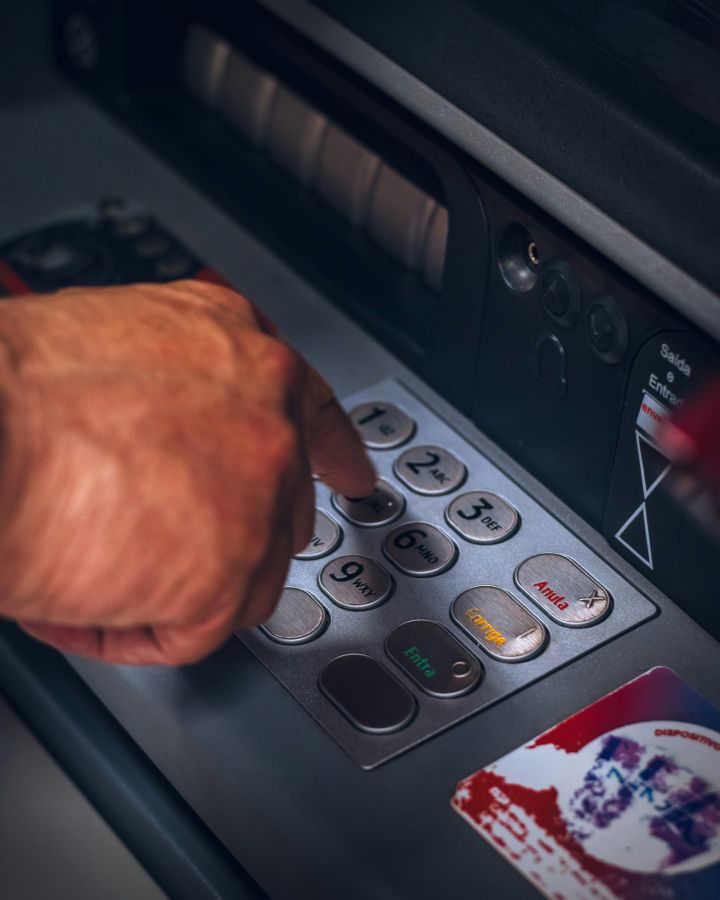 Hand die een code invoert op het numerieke toetsenblok van een geldautomaat met een zichtbare bankpas ernaast